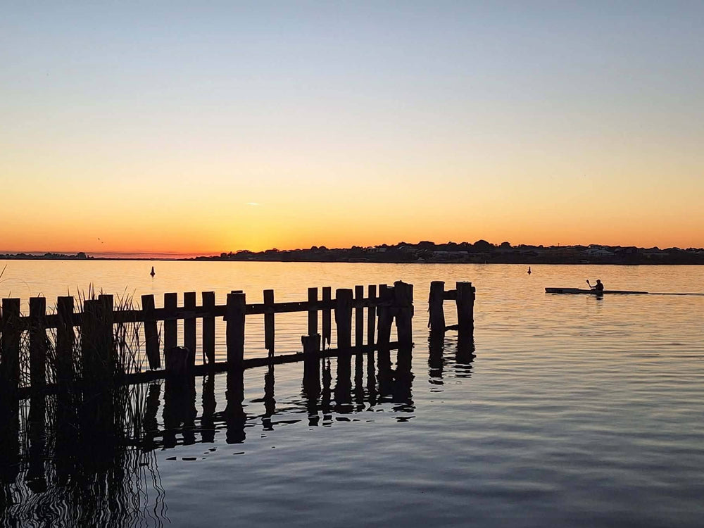 Golden sunset over calm water with old wooden jetty posts and a kayaker
