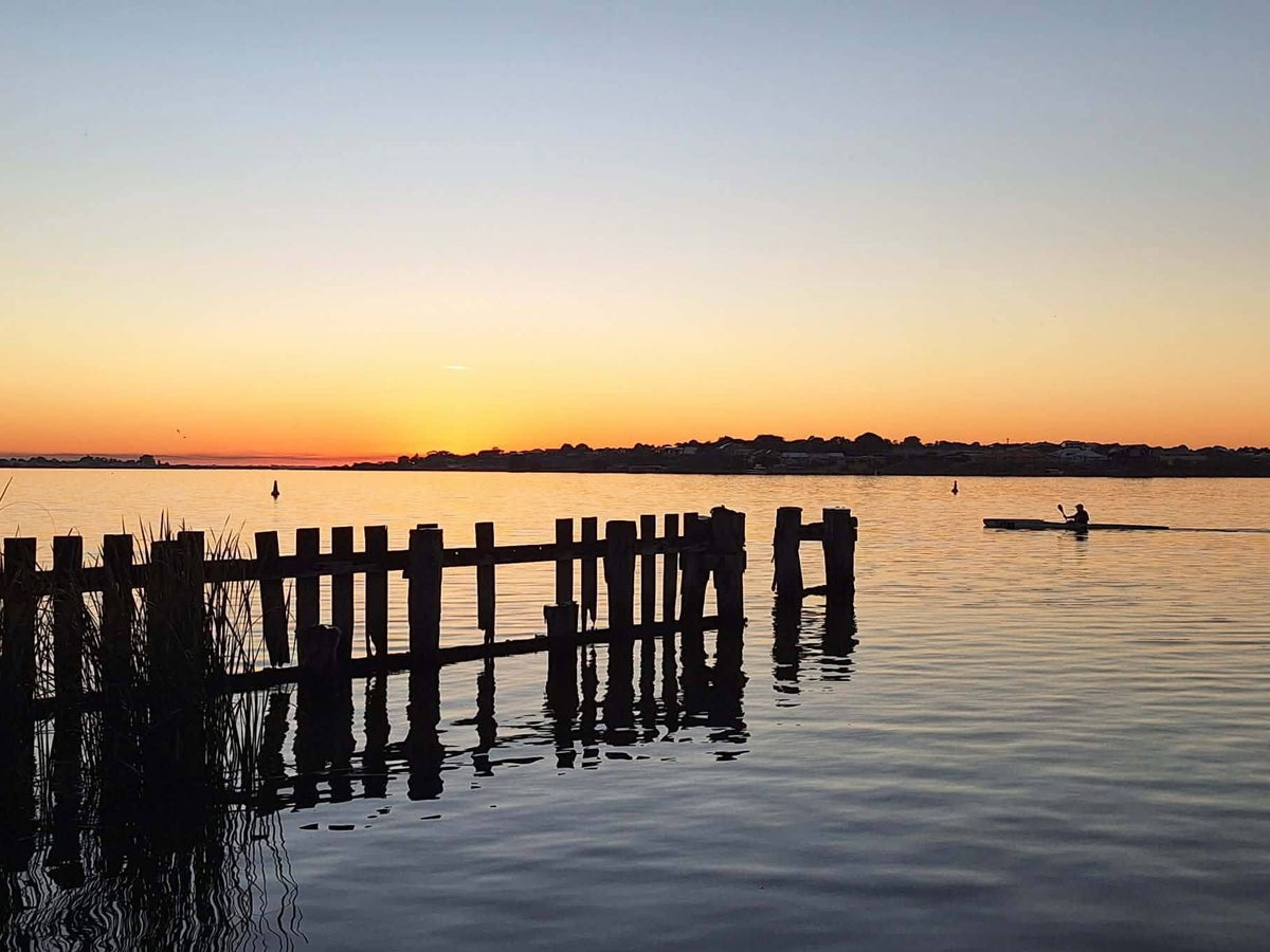 Golden sunset over calm water with old wooden jetty posts and a kayaker